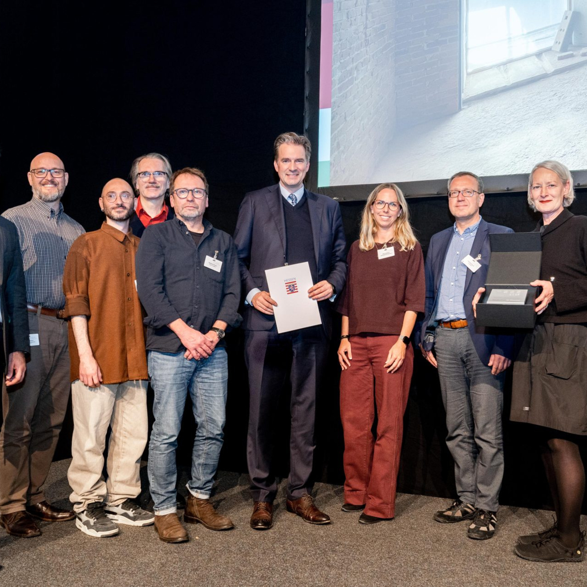 Große Bühne: Hessens Wohnungsbauminister Kaweh Mansoori (li.) übergibt den Hessischen Landespreis Baukultur 2025 für den Hochbunker Agathof im Beisein von Kassels Oberbürgermeister Sven Schoeller (Mi.) an Projektbeteiligte. 