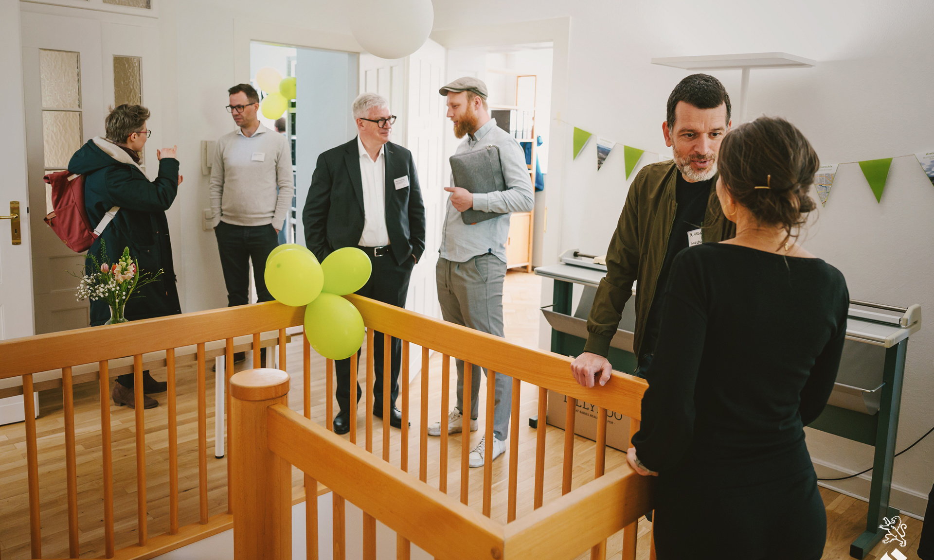 Mehrere Menschen unterhalten sich im ersten Stock des mit grünen Luftballons geschmückten neuen Bürogebäudes der ProjektStadt Weimar