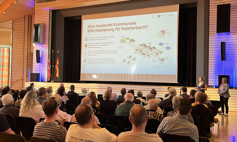 Die Bürger der Stadt Kelsterbach sitzen in einem Saal und schauen auf eine PowerPoint Präsentation.