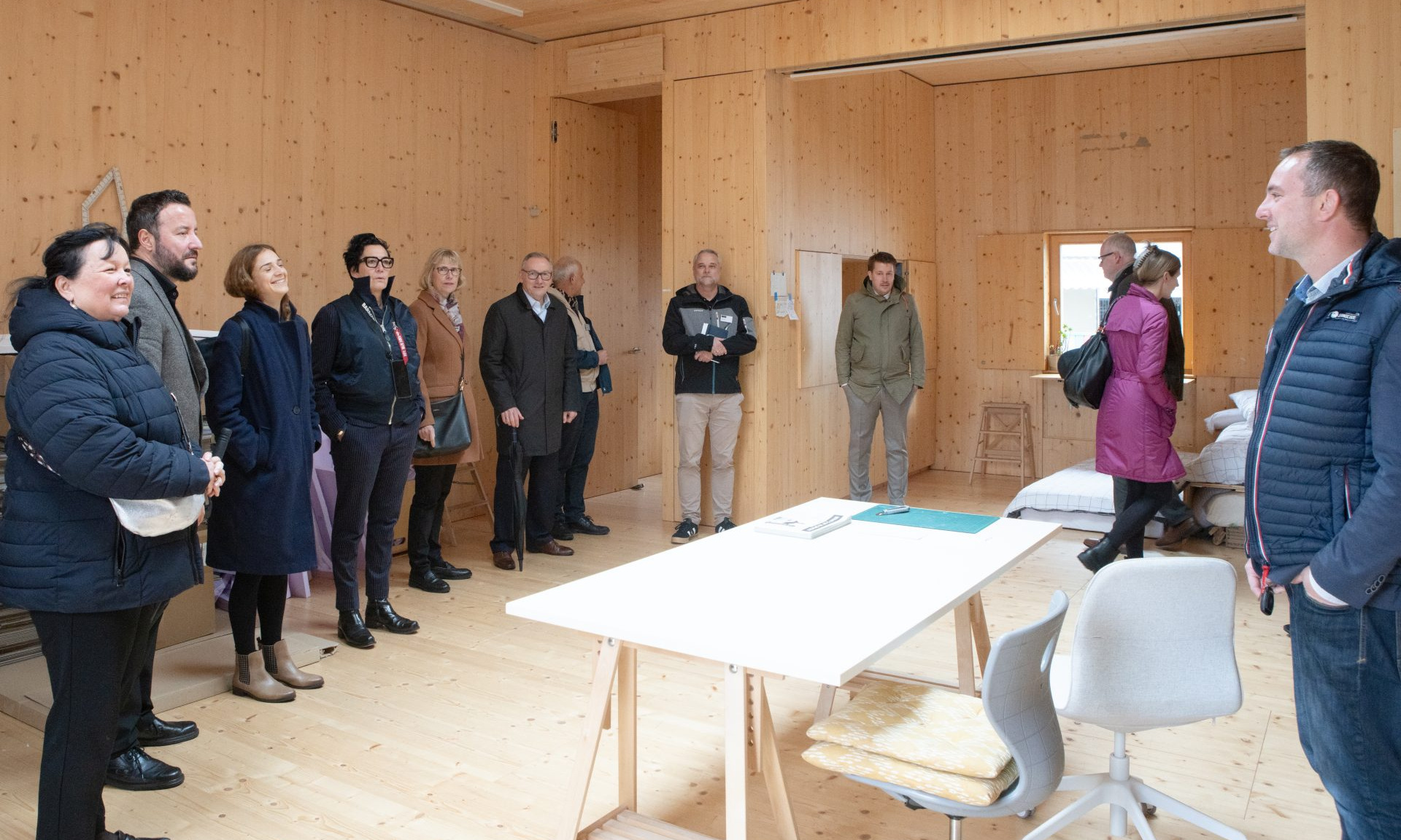 Mehrere Menschen in einem Raum, dessen Wände und Boden aus hellem Holz bestehen.
