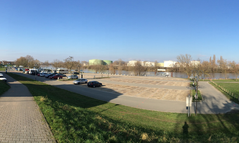 Totalaufnahme des Platzes. Zu sehen ist ein Parkplatz direkt am Fluss.