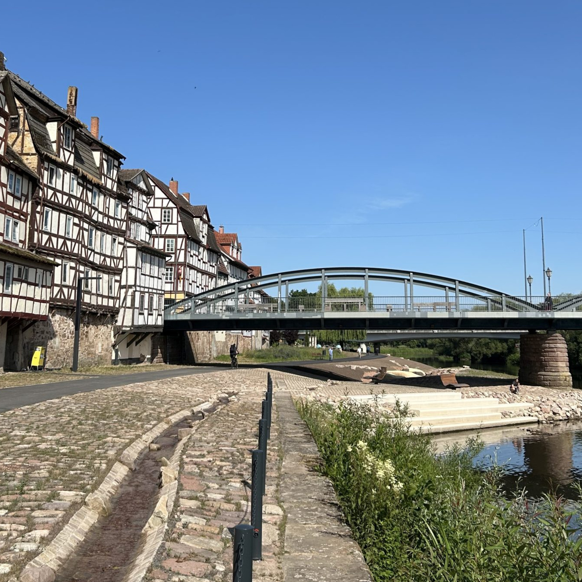 Neu gestalteter Uferbereich mit Bachlauf, rechts die Fulda, im Hintergrund Fachwerkhäuser und eine Brücke