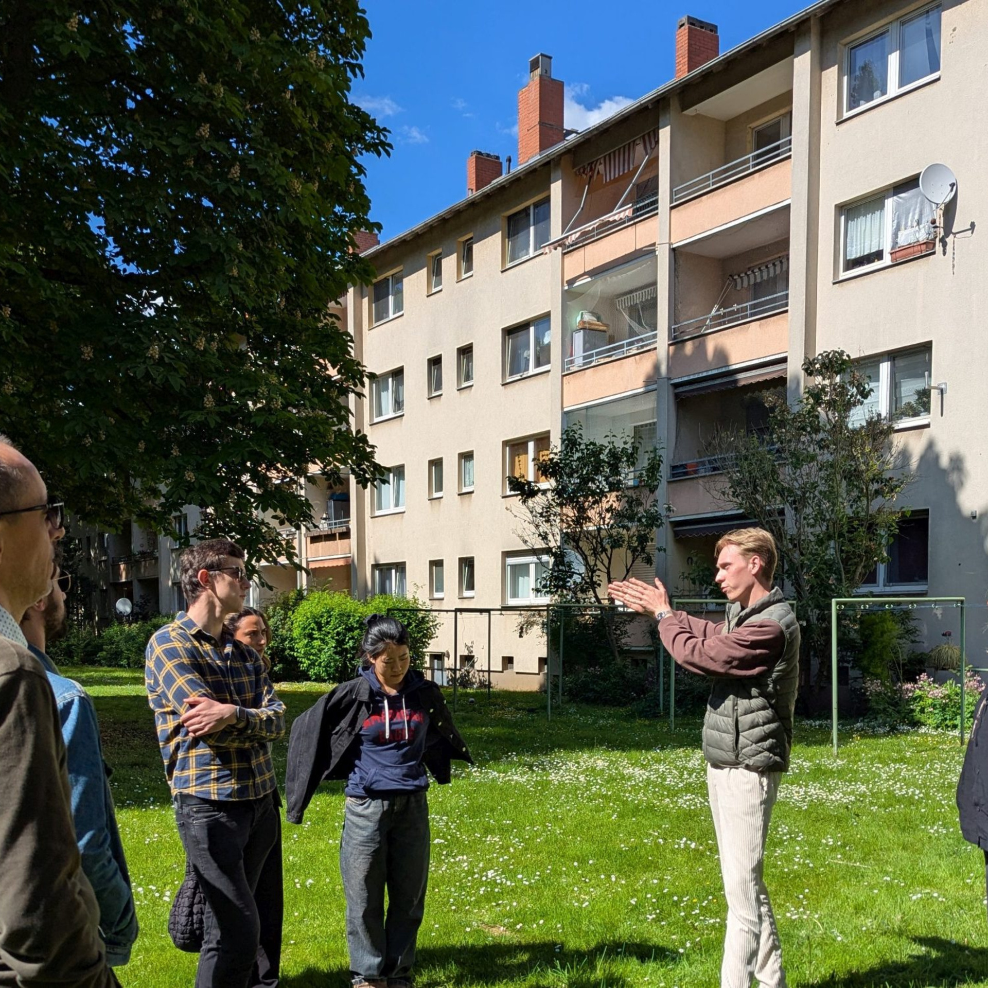Mehrere Studierende auf der Grünfläche vor einem Mehrfamilienhaus