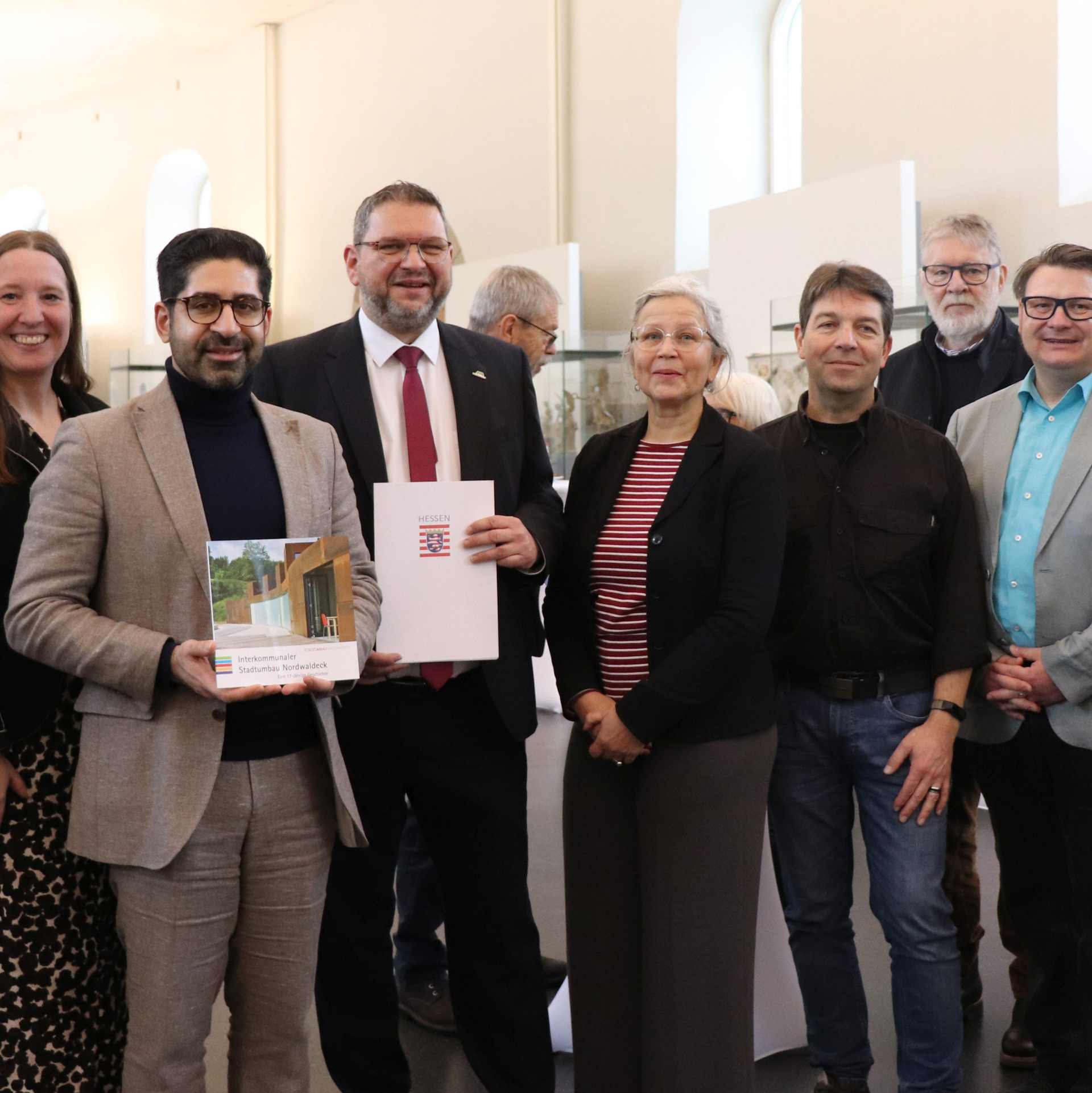 Minister Kaweh Mansoori übergibt den Förderbescheid an Bad Arolsens Bürgermeister Marko Lambion, beide sind umringt von weiteren Personen