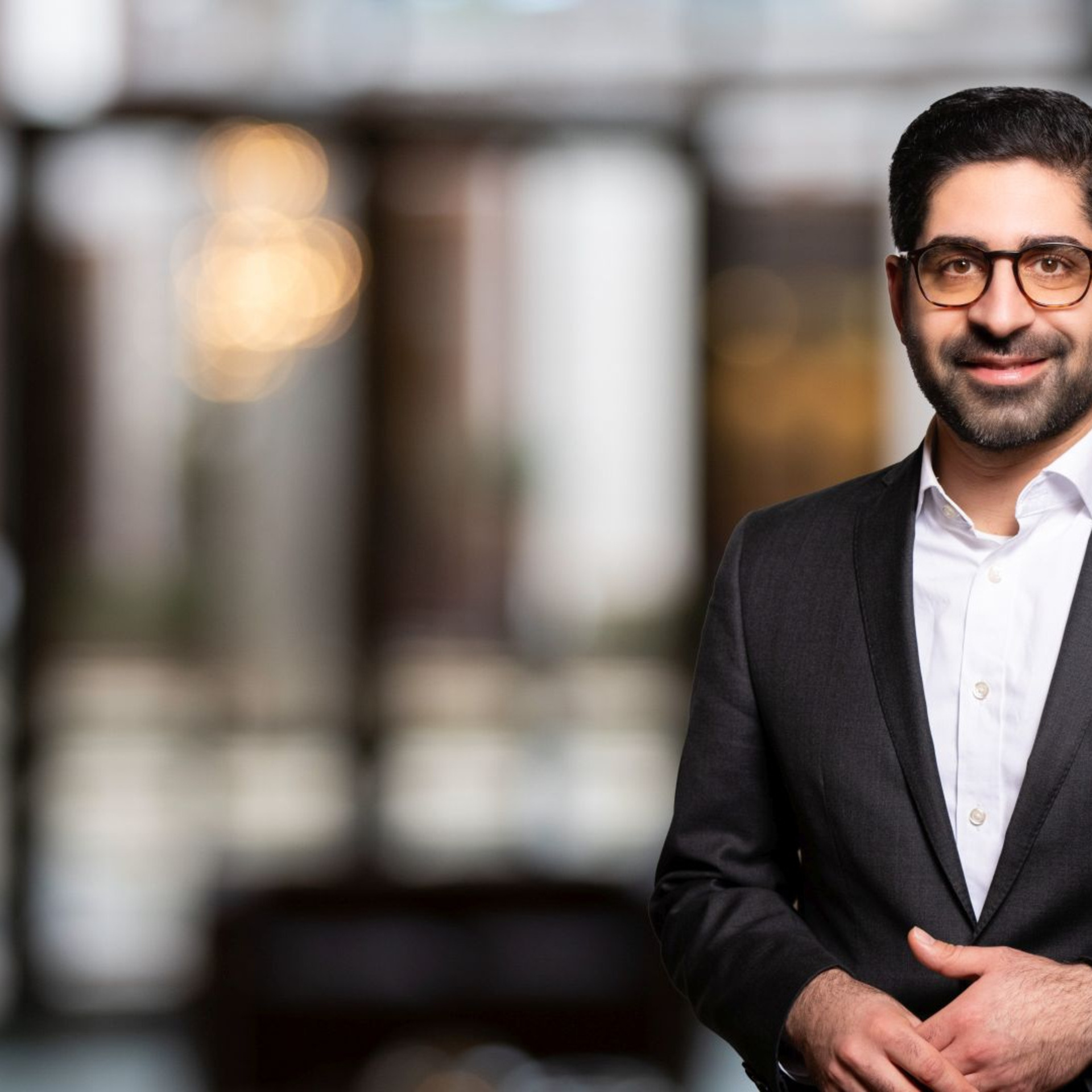 Kaweh Mansoori in einem schwarzen Anzug vor unscharfem Hintergrund.