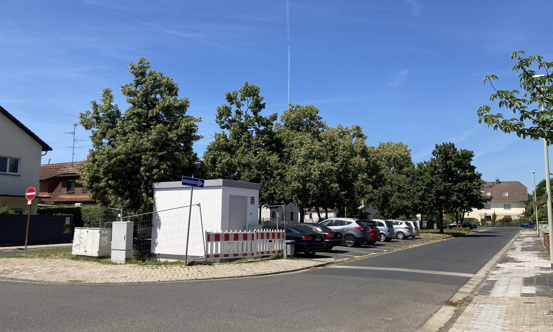 Blick auf einen Grünstreifen mit Baucontainer und parkenden Autos, im Vordergrund Straße