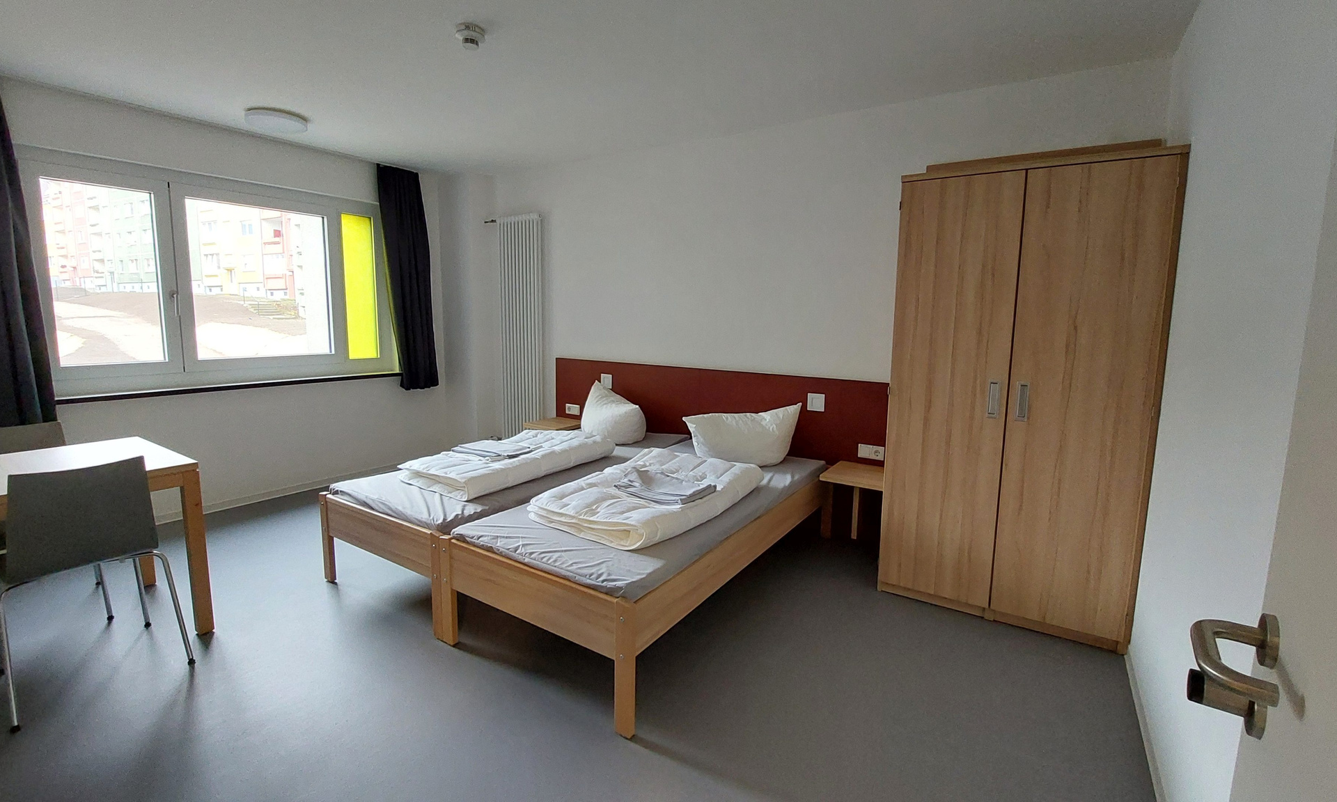Blick in ein Schlafzimmer der DJH Gotha mit Bett, Schrank und Tisch, im Hintergrund ein Fenster