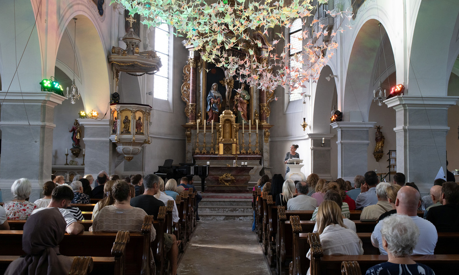 Innenraum der Herz-Jesu-Kirche Kelsterbach, von hinten aufgenommen, über den Besuchern "schwebt" ein Schwarm aus 843 Origami-Kranichen