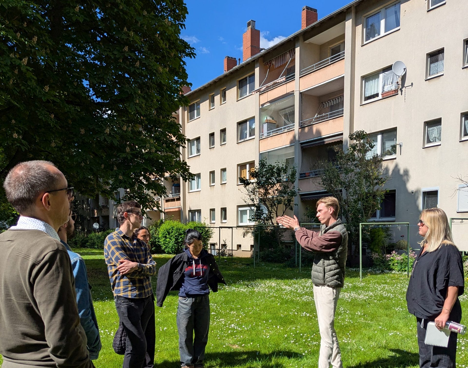 Mehrere Studierende auf der Grünfläche vor einem Mehrfamilienhaus